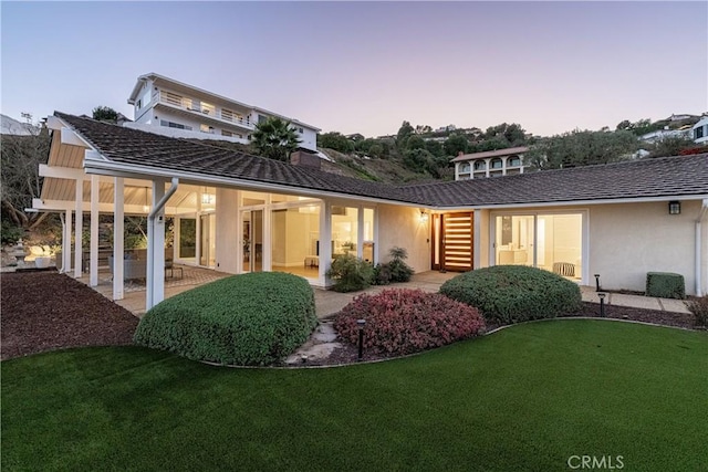 back house at dusk with a lawn and a patio area