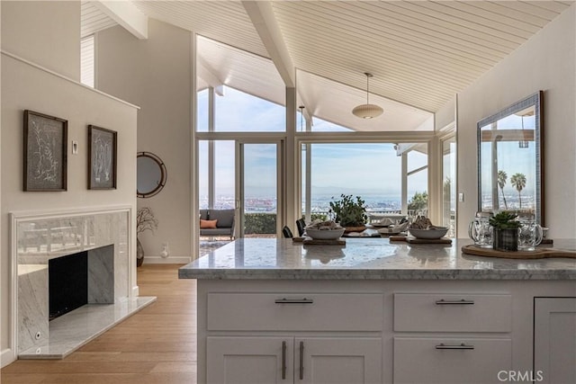 kitchen with light stone counters, a premium fireplace, beamed ceiling, and light wood-type flooring