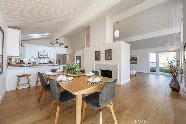 dining space with a high end fireplace, light hardwood / wood-style floors, and vaulted ceiling with beams