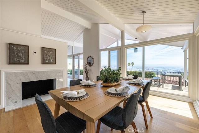 dining space with floor to ceiling windows, high vaulted ceiling, light hardwood / wood-style flooring, beamed ceiling, and a high end fireplace