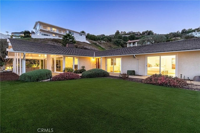 back house at dusk featuring a lawn