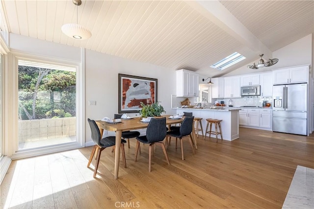 dining area featuring wood ceiling, lofted ceiling with skylight, sink, and light wood-type flooring