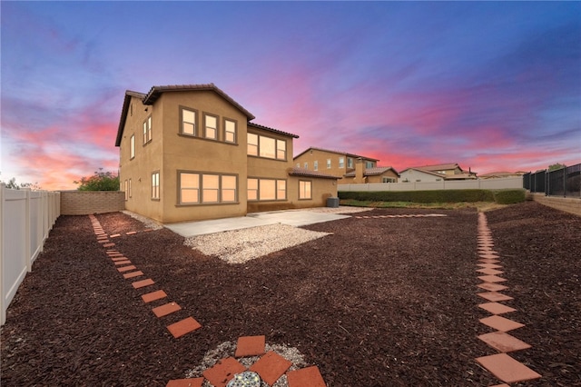 back of house at dusk with a fenced backyard, stucco siding, a tiled roof, and a patio