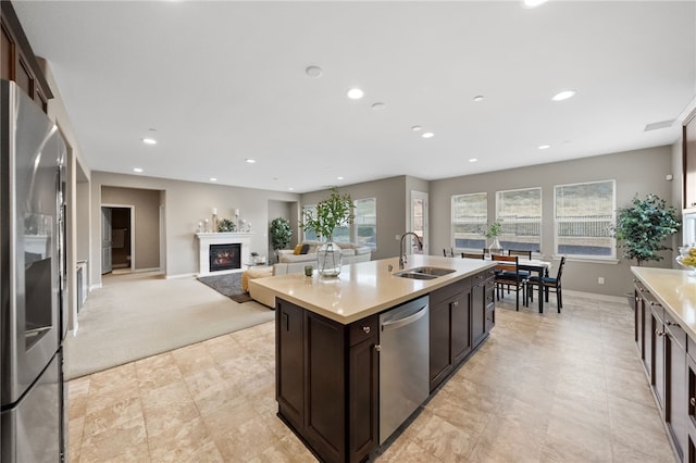 kitchen with light countertops, stainless steel appliances, recessed lighting, a sink, and a glass covered fireplace