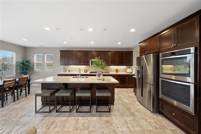 kitchen with a breakfast bar, light countertops, dark brown cabinets, and appliances with stainless steel finishes