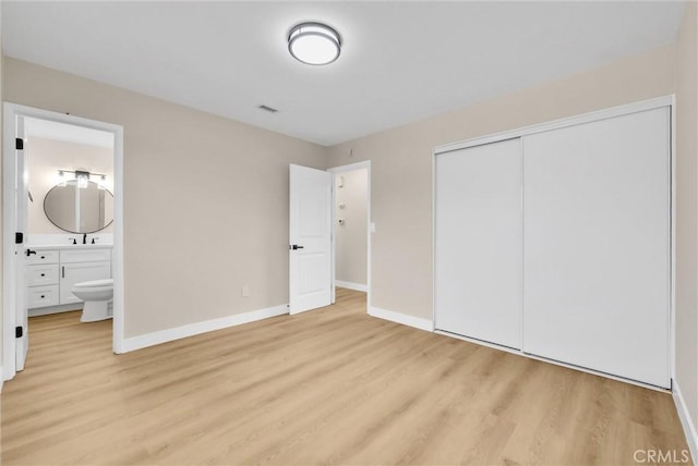 unfurnished bedroom with a closet, sink, ensuite bath, and light hardwood / wood-style flooring