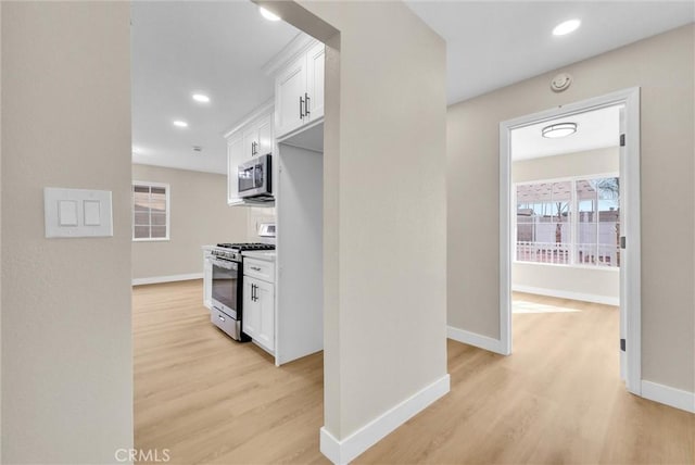 kitchen with appliances with stainless steel finishes, light hardwood / wood-style flooring, and white cabinets