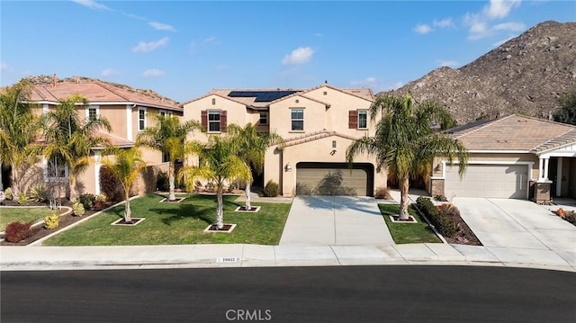 view of front of property featuring a garage, a mountain view, solar panels, and a front lawn