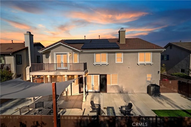 back house at dusk featuring solar panels, a patio, and a balcony