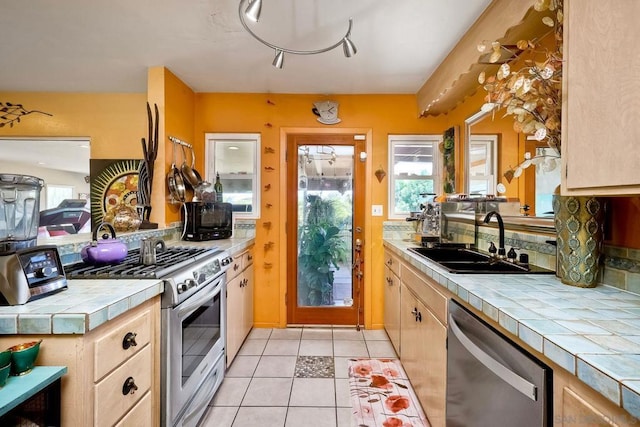 kitchen with tile countertops, sink, decorative backsplash, light tile patterned floors, and stainless steel appliances