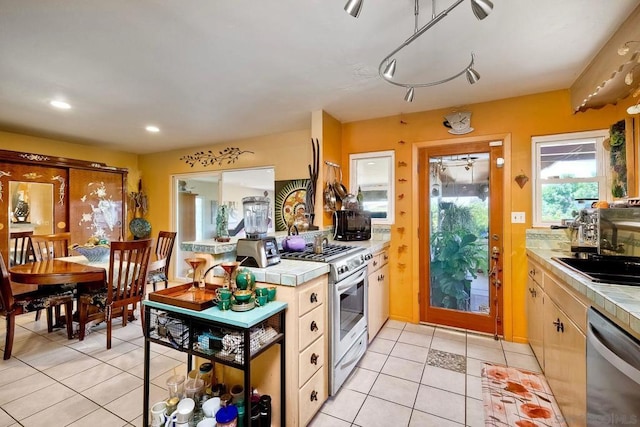 kitchen with sink, light tile patterned floors, tile counters, and appliances with stainless steel finishes