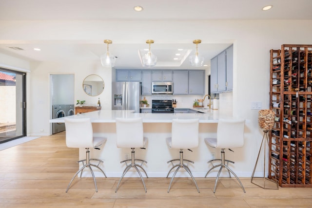 kitchen featuring a kitchen bar, washing machine and clothes dryer, kitchen peninsula, stainless steel appliances, and light wood-type flooring