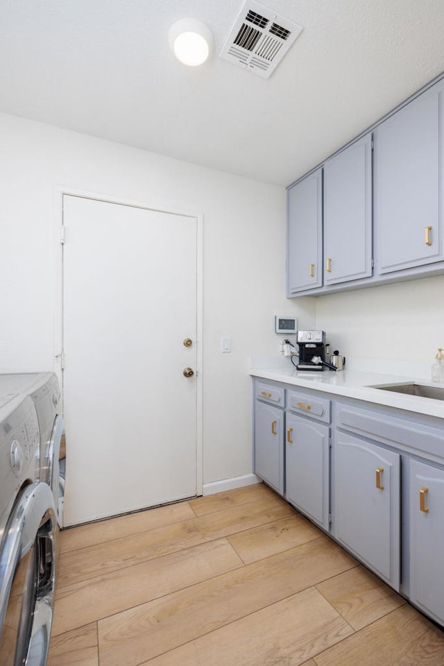 laundry area featuring cabinets, washer and clothes dryer, sink, and light hardwood / wood-style flooring