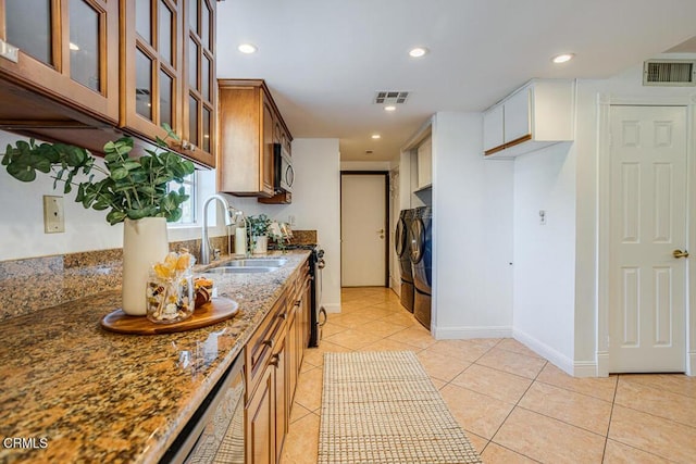 kitchen with sink, light tile patterned floors, washer and clothes dryer, stainless steel appliances, and stone countertops