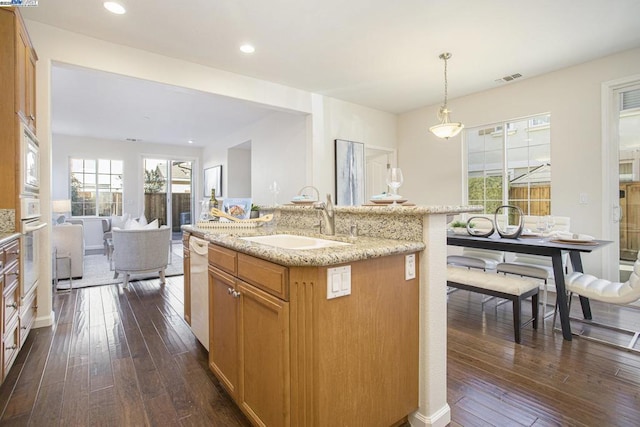 kitchen featuring sink, dark hardwood / wood-style flooring, hanging light fixtures, a kitchen island with sink, and white appliances