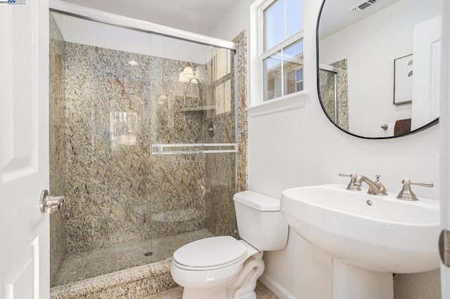 bathroom featuring toilet, a shower with shower door, and sink