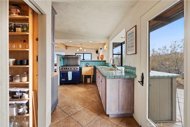 kitchen featuring vaulted ceiling, stainless steel stove, sink, backsplash, and tile counters