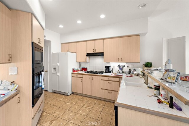 kitchen featuring sink, backsplash, white fridge with ice dispenser, stainless steel gas cooktop, and light brown cabinets