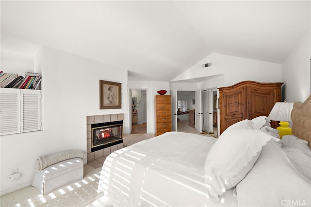 carpeted bedroom with a tiled fireplace and vaulted ceiling