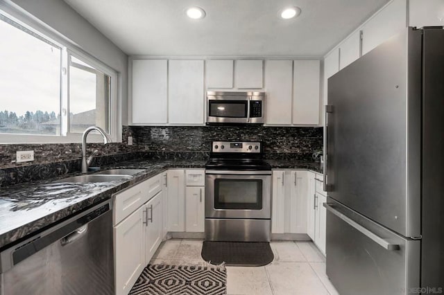 kitchen with light tile patterned flooring, sink, white cabinetry, appliances with stainless steel finishes, and dark stone counters