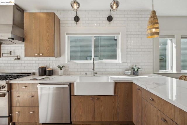 kitchen featuring sink, appliances with stainless steel finishes, pendant lighting, decorative backsplash, and wall chimney range hood