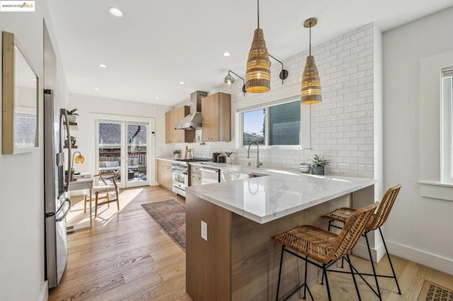 kitchen featuring a breakfast bar, hanging light fixtures, light hardwood / wood-style floors, kitchen peninsula, and wall chimney range hood