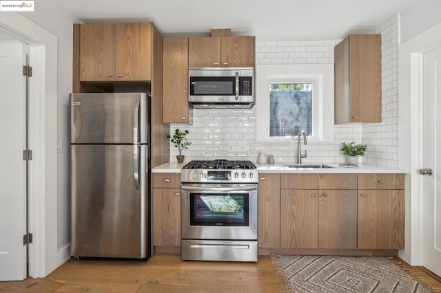 kitchen featuring appliances with stainless steel finishes, sink, light wood-type flooring, and decorative backsplash