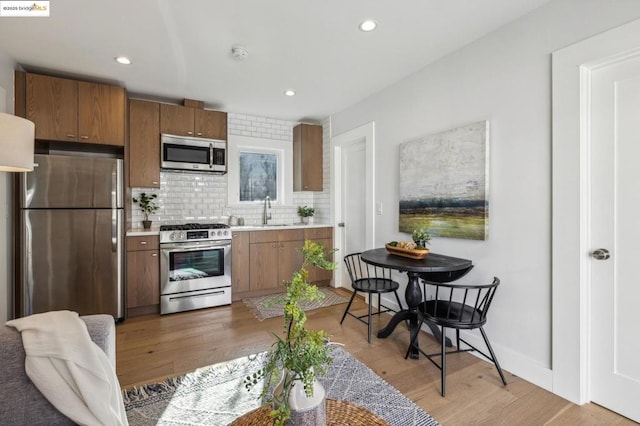 kitchen with appliances with stainless steel finishes, sink, backsplash, and light hardwood / wood-style flooring