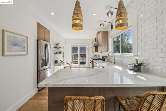 kitchen featuring sink, light wood-type flooring, kitchen peninsula, stainless steel appliances, and decorative backsplash