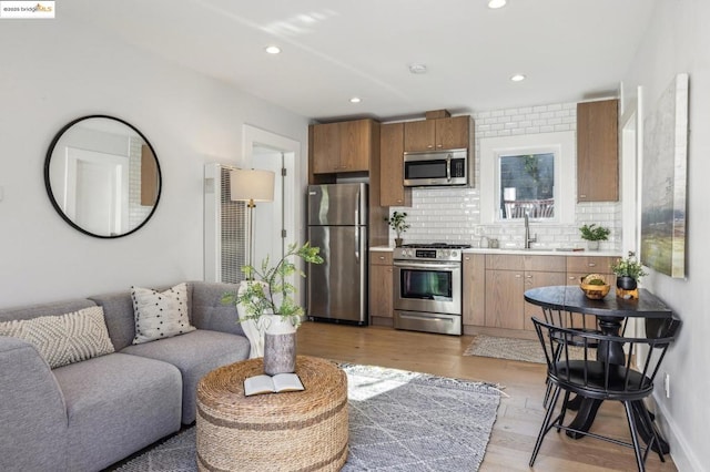 kitchen with tasteful backsplash, appliances with stainless steel finishes, sink, and light hardwood / wood-style flooring