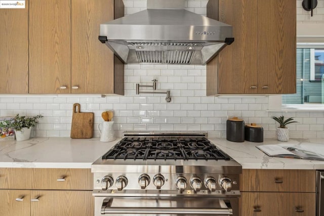 kitchen with backsplash, light stone countertops, high end stove, and wall chimney range hood