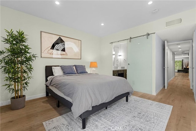 bedroom featuring ensuite bathroom, a barn door, and light hardwood / wood-style floors