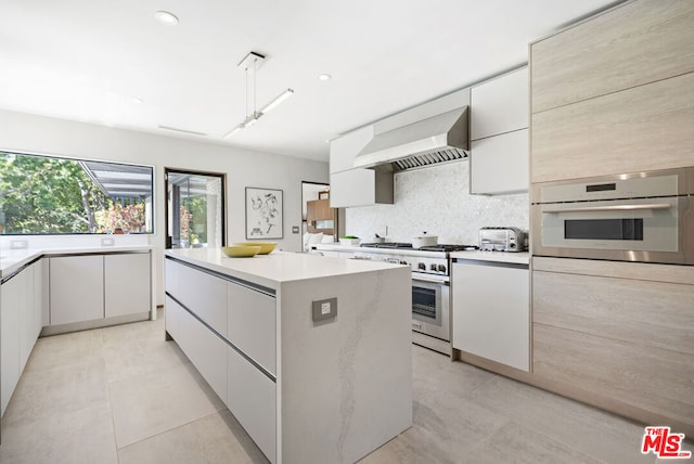 kitchen with white cabinetry, a center island, appliances with stainless steel finishes, decorative backsplash, and wall chimney range hood