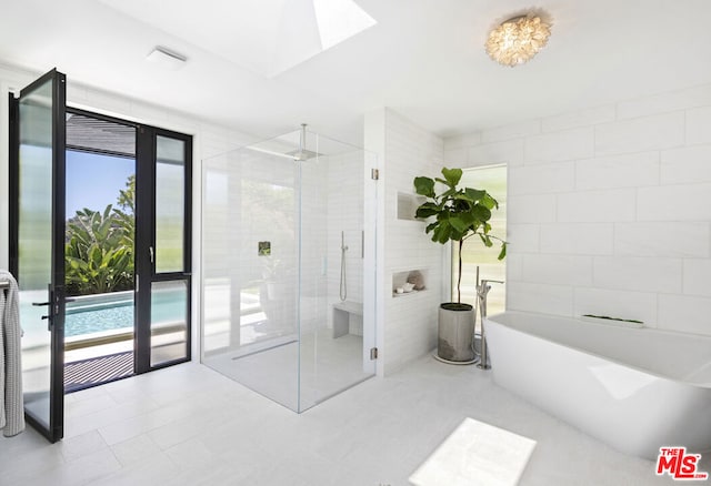 bathroom featuring shower with separate bathtub, tile walls, and a skylight