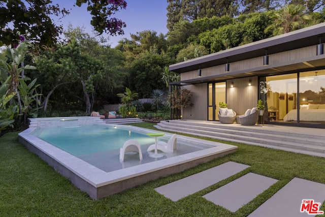 pool at dusk featuring outdoor lounge area and a lawn