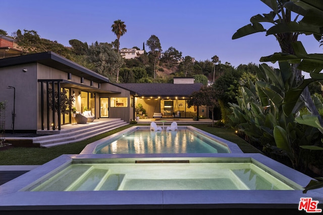 pool at dusk with an in ground hot tub and a patio area