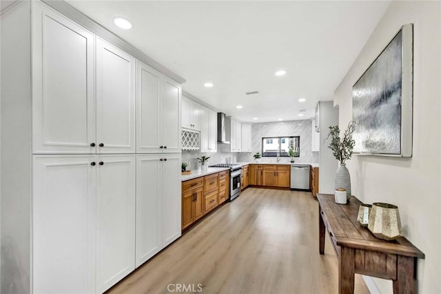 kitchen with wall chimney exhaust hood, stainless steel appliances, light countertops, and recessed lighting