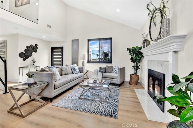 living area with high vaulted ceiling, a premium fireplace, wood finished floors, visible vents, and baseboards