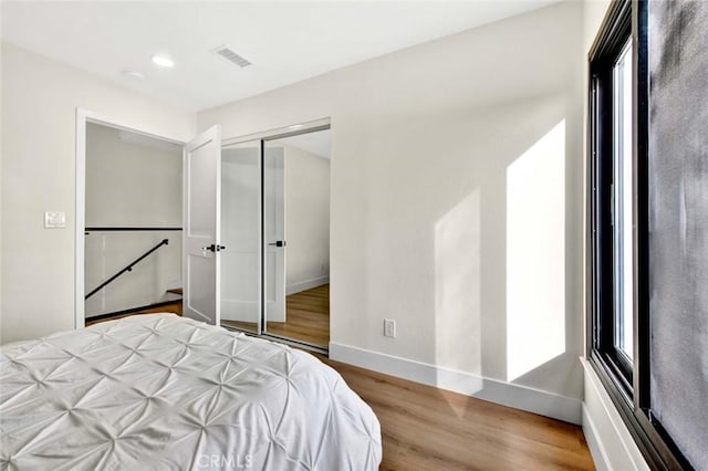 bedroom with a closet, visible vents, baseboards, and wood finished floors