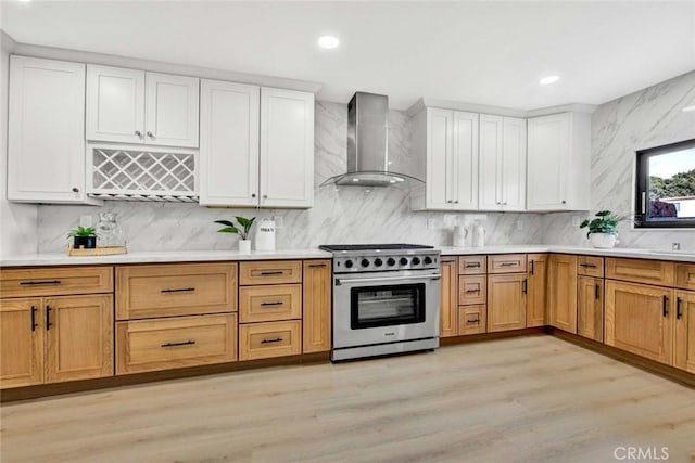 kitchen with high end stove, light wood-style floors, light countertops, decorative backsplash, and wall chimney exhaust hood