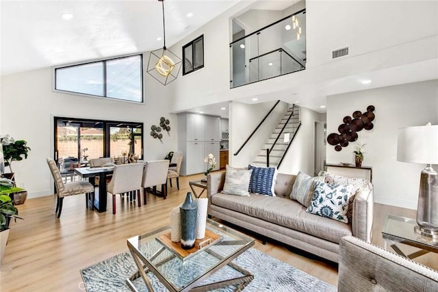 living area featuring light wood finished floors, baseboards, visible vents, a towering ceiling, and stairway