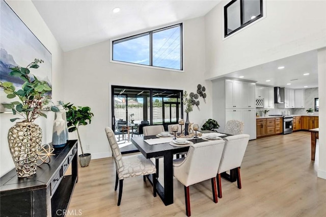 dining area featuring a towering ceiling, light wood finished floors, baseboards, and recessed lighting