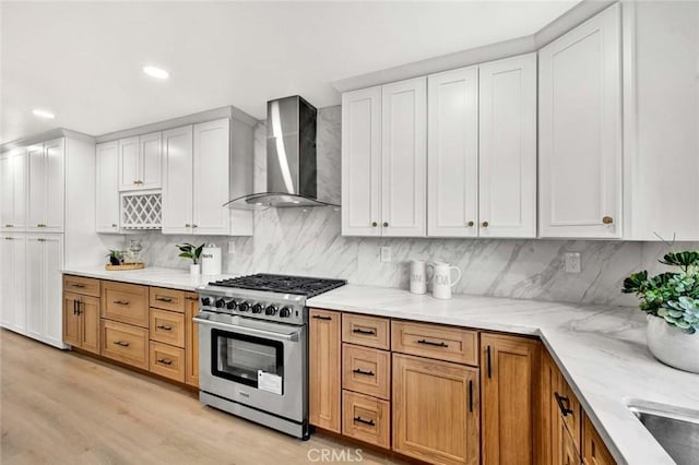 kitchen with light wood-type flooring, wall chimney exhaust hood, light stone countertops, high end stove, and backsplash