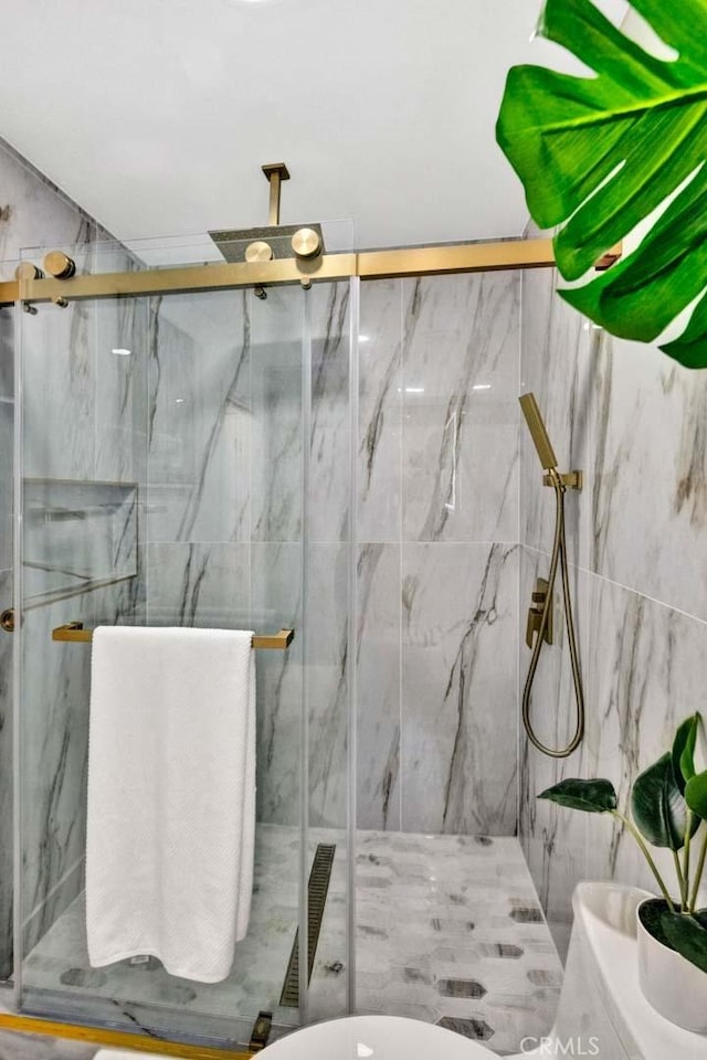 full bathroom with a marble finish shower, toilet, and tile walls