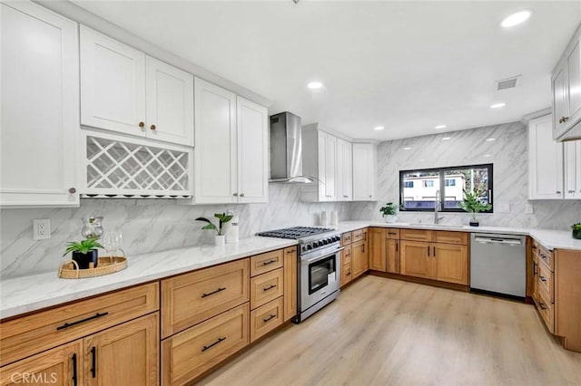 kitchen with white cabinetry, sink, wall chimney exhaust hood, stainless steel appliances, and light hardwood / wood-style flooring