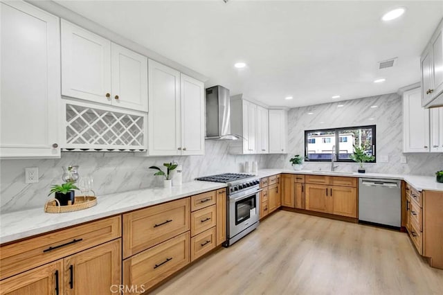 kitchen featuring visible vents, appliances with stainless steel finishes, a sink, wall chimney range hood, and light wood-type flooring