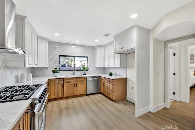 kitchen featuring wall chimney range hood, light wood-style floors, stainless steel appliances, and a sink