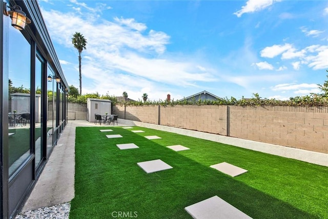 view of yard featuring a fenced backyard, a storage unit, and an outbuilding