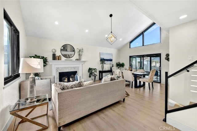 living room with a tiled fireplace, stairs, light wood-type flooring, high vaulted ceiling, and recessed lighting