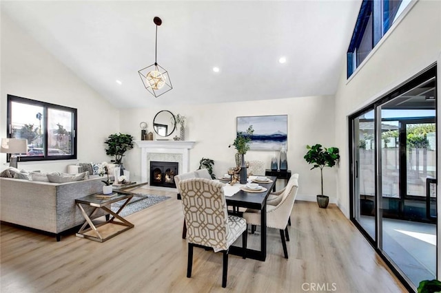 dining space with light wood-type flooring, a fireplace with flush hearth, high vaulted ceiling, and recessed lighting